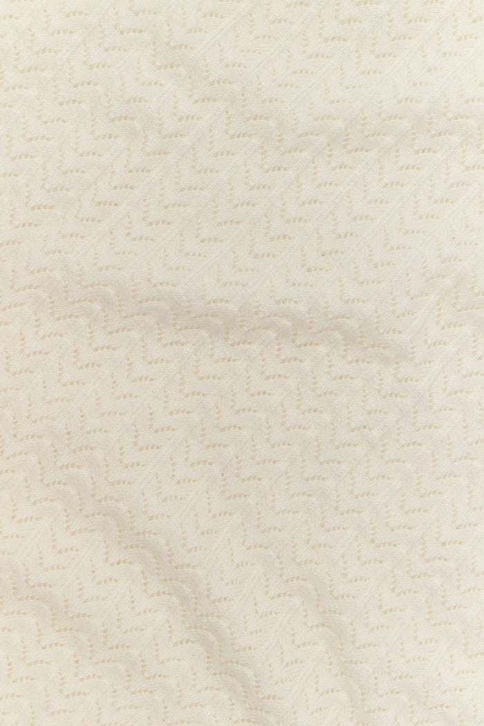A woman wearing the Roller Rabbit Chain Pointelle Lauren Sweater in cream and white pants, standing against a white background.
