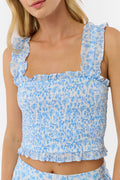 A woman wears the Roller Rabbit Cherry Blossom Toile Sabrina Top—a light blue and white floral smocked crop with ruffled straps and a square neckline. Only her upper body is shown against a plain background.