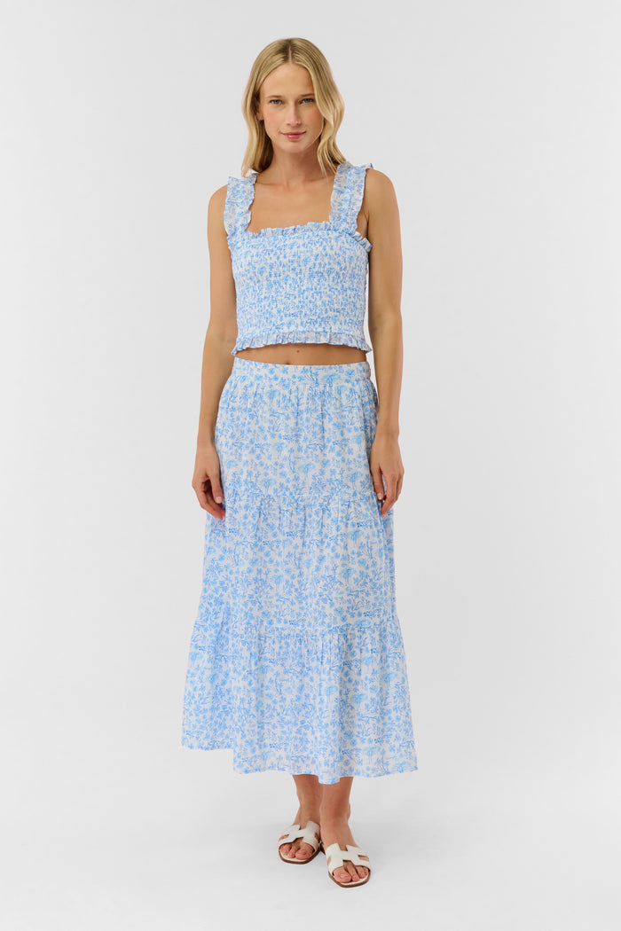 A woman wears the Roller Rabbit Cherry Blossom Toile Sabrina Top—a light blue and white floral smocked crop with ruffled straps and a square neckline. Only her upper body is shown against a plain background.
