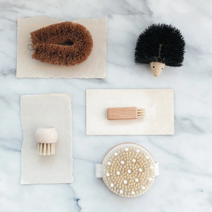 A collection of different brushes, including a cherry wood body brush, some on paper, and all of them on a marble surface.