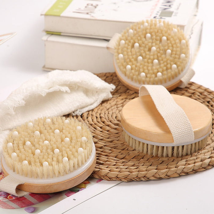Several round body brushes on a white surface with other items such as books and a white washcloth.