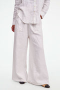 A person wearing Roller Rabbit's Chester Pant—loose-fitting linen wide leg pants with an elastic waist—paired with a matching white button-up shirt and two-tone black and beige flats, shown from shoulders to feet with one hand in their pocket.