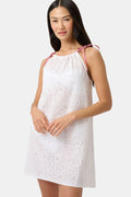 A woman models the Roller Rabbit Clover Eyelet Caroline Cover Up, a white cotton dress with adjustable shoulder straps and red gingham ties, set against a plain light gray background.