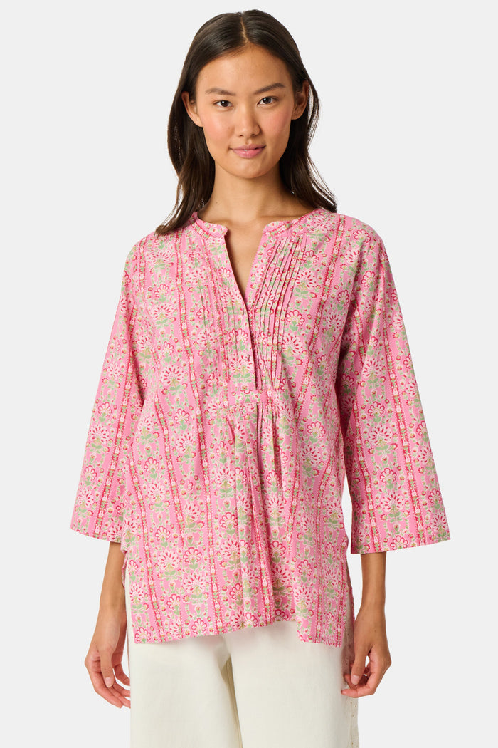 A woman wearing the Roller Rabbit Cora Floral Stripe Pippa Dress—a pink, short-sleeve, midi-length cotton dress with ruffled shoulders and a floral pattern—stands facing forward against a plain white background.