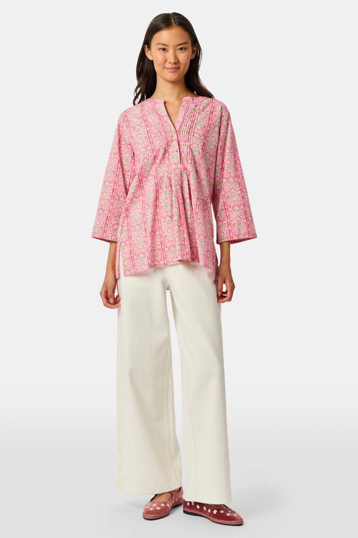 A woman wearing the Roller Rabbit Cora Floral Stripe Pippa Dress—a pink, short-sleeve, midi-length cotton dress with ruffled shoulders and a floral pattern—stands facing forward against a plain white background.