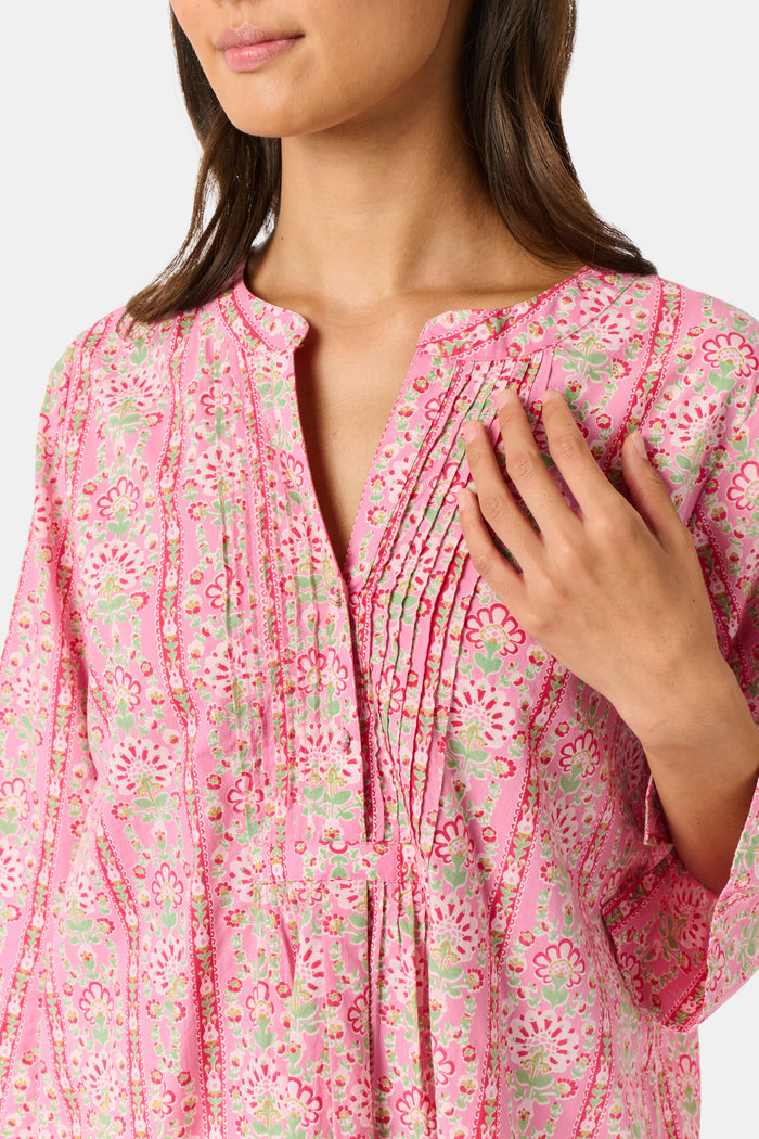 A woman wearing the Roller Rabbit Cora Floral Stripe Pippa Dress—a pink, short-sleeve, midi-length cotton dress with ruffled shoulders and a floral pattern—stands facing forward against a plain white background.