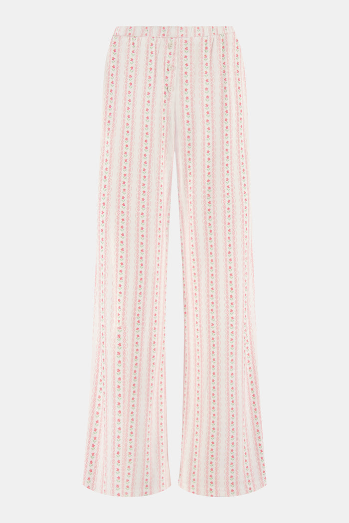 The Daisy Heart Stripe Boden Pant by Roller Rabbit features a wide-leg silhouette with a white base, adorned with vertical pink floral and dotted stripes. Designed for comfort, these pajama pants have an elastic waistband and are crafted from soft Pima cotton for a luxurious feel.