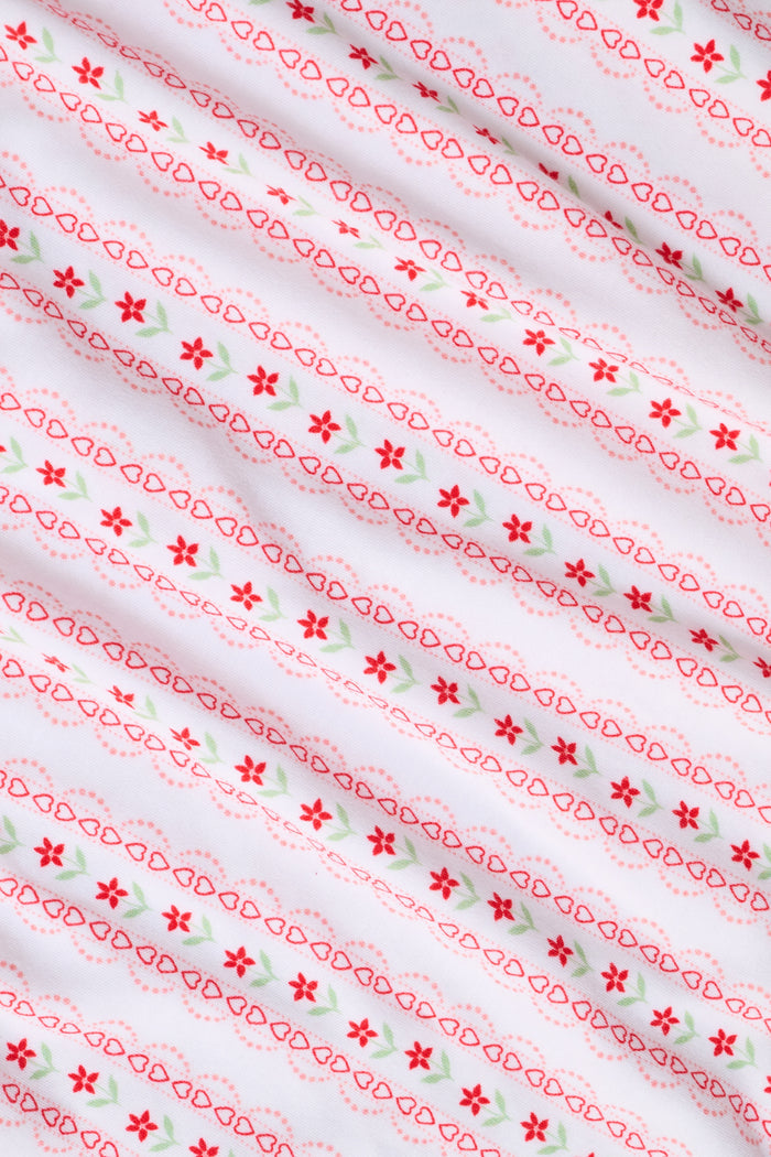 A woman smiles while wearing the Roller Rabbit Daisy Heart Stripe Jessie Long Sleeve Tee, a soft Pima cotton top adorned with pink and red daisies, paired with matching pajama bottoms, against a plain white background.