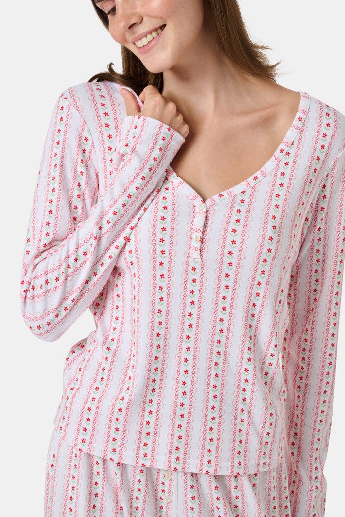 A woman smiles while wearing the Roller Rabbit Daisy Heart Stripe Jessie Long Sleeve Tee, a soft Pima cotton top adorned with pink and red daisies, paired with matching pajama bottoms, against a plain white background.