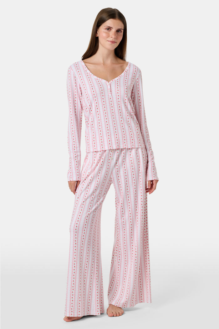 A woman smiles while wearing the Roller Rabbit Daisy Heart Stripe Jessie Long Sleeve Tee, a soft Pima cotton top adorned with pink and red daisies, paired with matching pajama bottoms, against a plain white background.