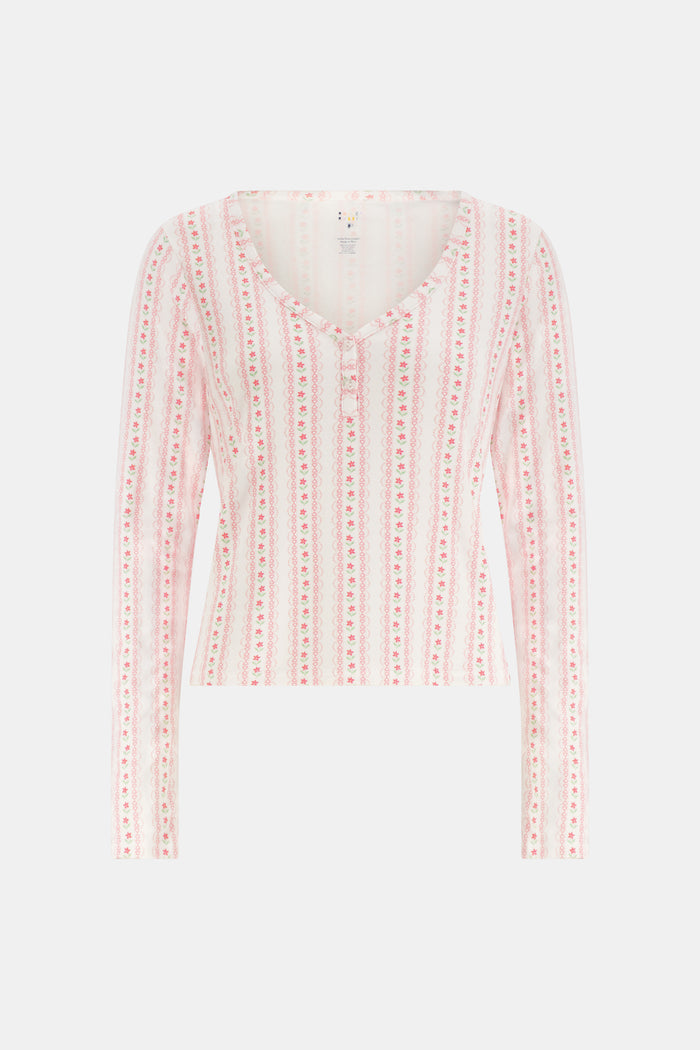 A woman smiles while wearing the Roller Rabbit Daisy Heart Stripe Jessie Long Sleeve Tee, a soft Pima cotton top adorned with pink and red daisies, paired with matching pajama bottoms, against a plain white background.