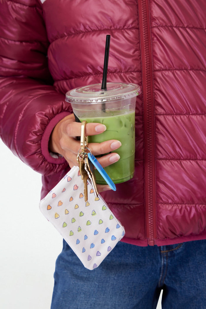 Keep essentials secure with the Roller Rabbit Disco Hearts Coin Pouch—a small white cotton canvas pouch featuring a gold clip and a colorful, hand-drawn heart pattern. Water-resistant for everyday use.