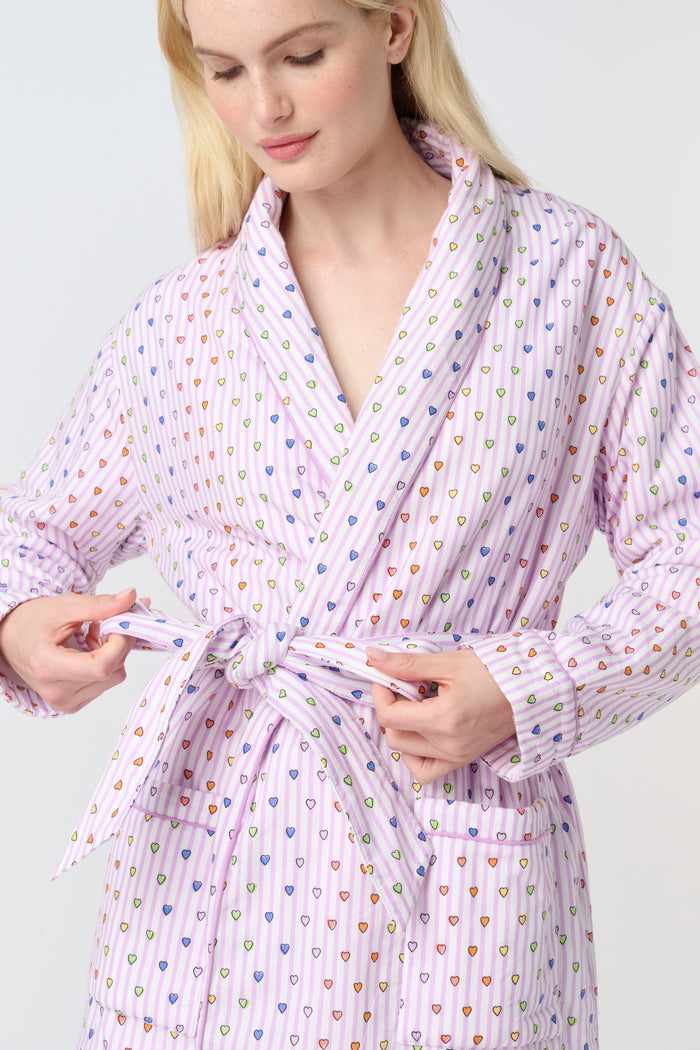 A person with long blonde hair stands barefoot against a plain white background, wearing the Roller Rabbit Disco Hearts Cosmo Robe with a belt tied at the waist.