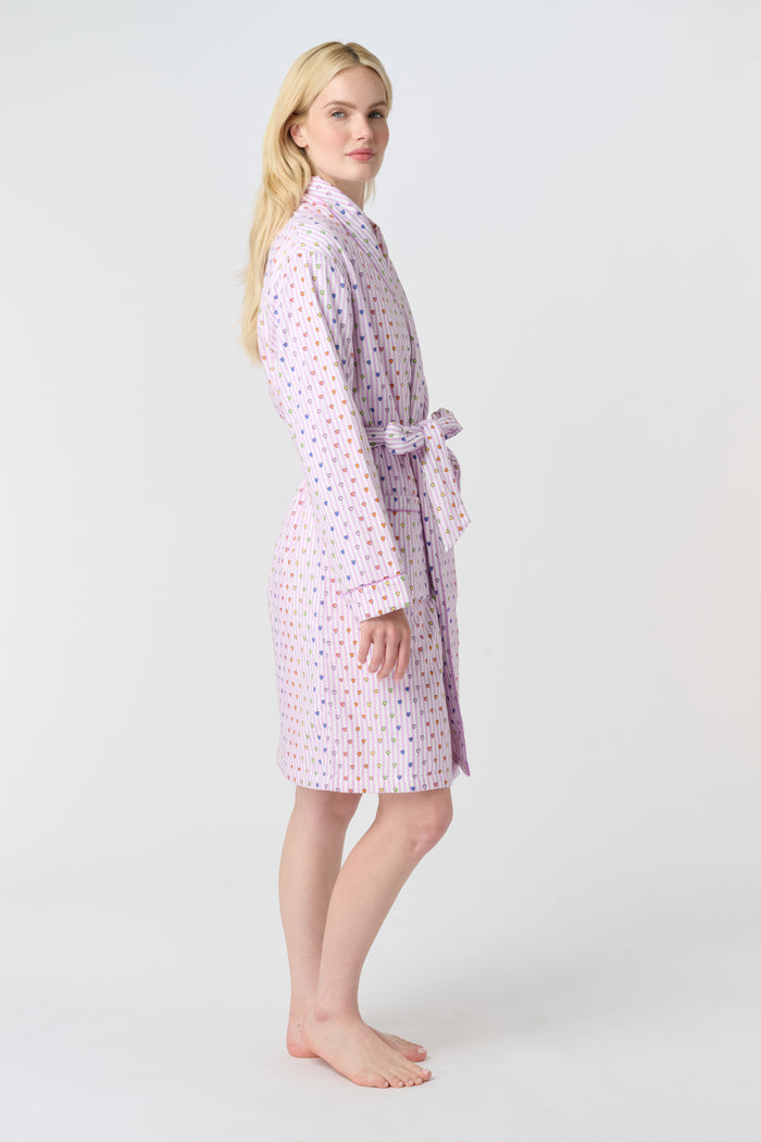 A person with long blonde hair stands barefoot against a plain white background, wearing the Roller Rabbit Disco Hearts Cosmo Robe with a belt tied at the waist.