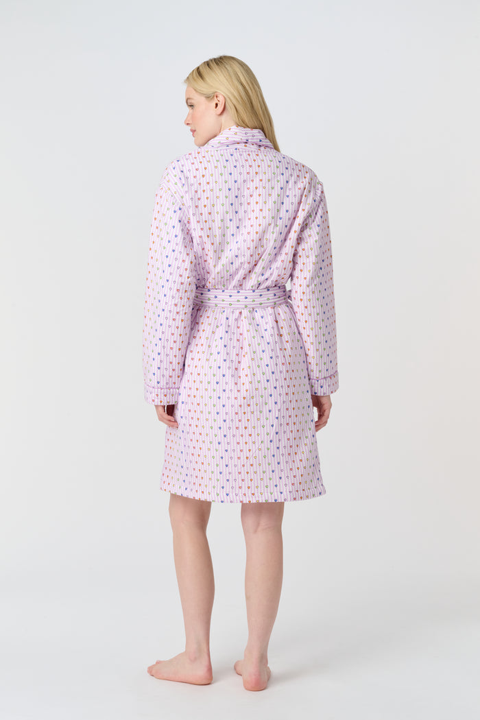 A person with long blonde hair stands barefoot against a plain white background, wearing the Roller Rabbit Disco Hearts Cosmo Robe with a belt tied at the waist.