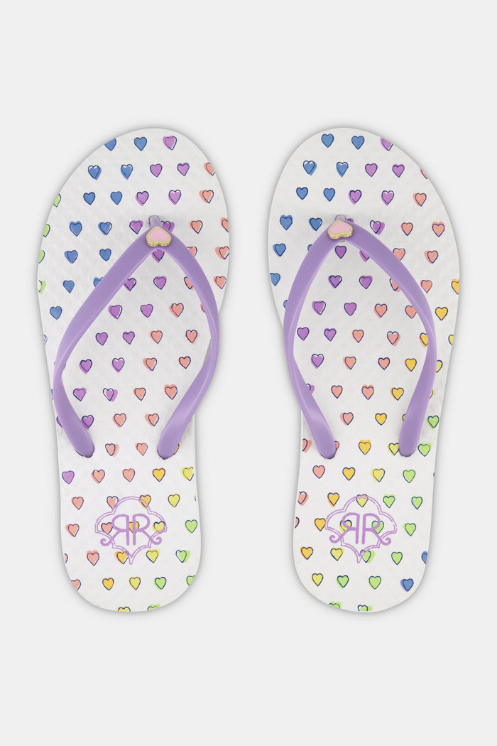 Roller Rabbit's Disco Hearts Flip Flops feature a colorful heart pattern and light purple straps, making them the perfect vacation footwear. Shown here against a plain white background.