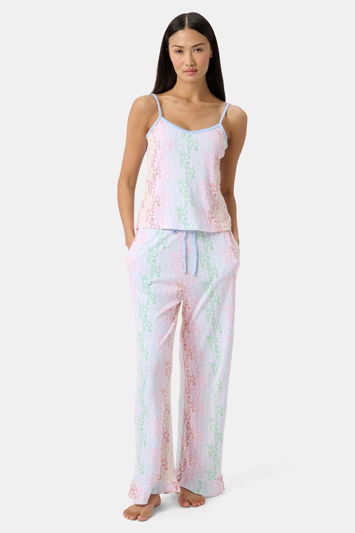 A woman stands barefoot wearing the Roller Rabbit Disco Monkey Lily Set, a matching Pima cotton pajama set featuring a pastel lace-like pattern, sleeveless camisole top, and drawstring pants with pockets.