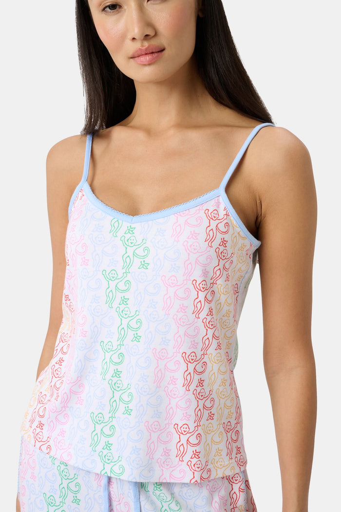 A woman stands barefoot wearing the Roller Rabbit Disco Monkey Lily Set, a matching Pima cotton pajama set featuring a pastel lace-like pattern, sleeveless camisole top, and drawstring pants with pockets.