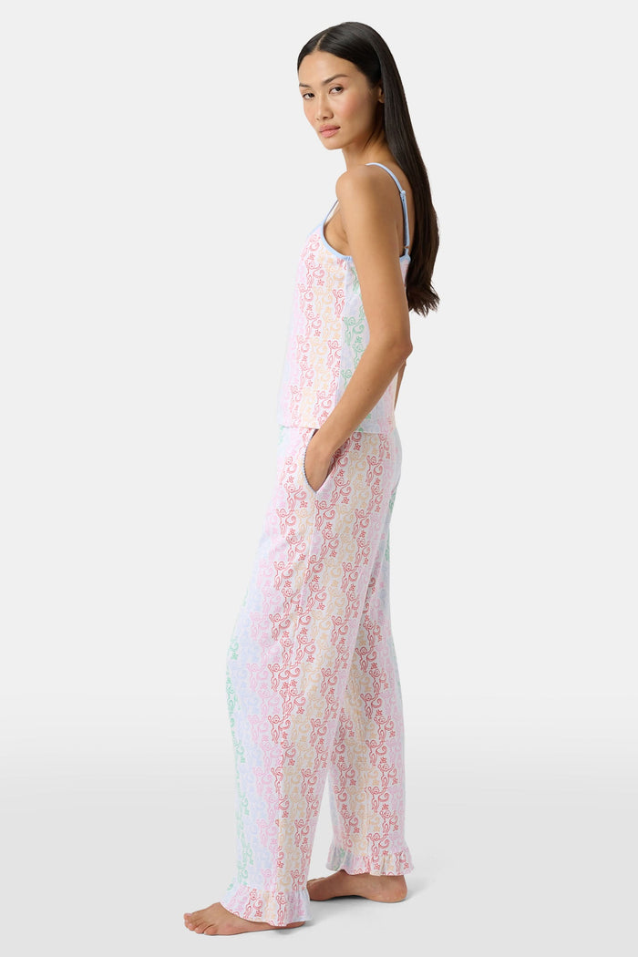A woman stands barefoot wearing the Roller Rabbit Disco Monkey Lily Set, a matching Pima cotton pajama set featuring a pastel lace-like pattern, sleeveless camisole top, and drawstring pants with pockets.
