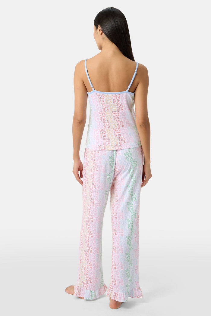 A woman stands barefoot wearing the Roller Rabbit Disco Monkey Lily Set, a matching Pima cotton pajama set featuring a pastel lace-like pattern, sleeveless camisole top, and drawstring pants with pockets.