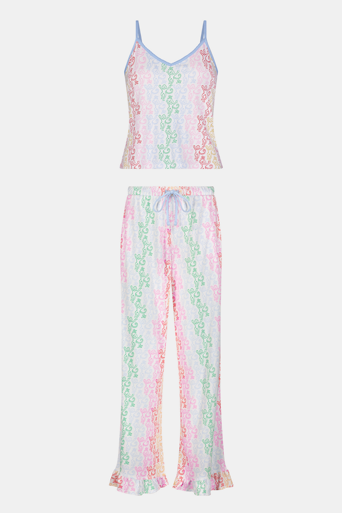 A woman stands barefoot wearing the Roller Rabbit Disco Monkey Lily Set, a matching Pima cotton pajama set featuring a pastel lace-like pattern, sleeveless camisole top, and drawstring pants with pockets.