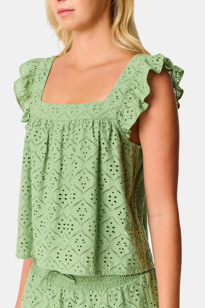 A person wearing the Roller Rabbit Elsa Eyelet Peyton Skirt in sage green, featuring a cotton eyelet fabric, ruffled hem, and elastic waistband, paired with a matching top and slightly lifting the top to reveal the skirt’s waist.