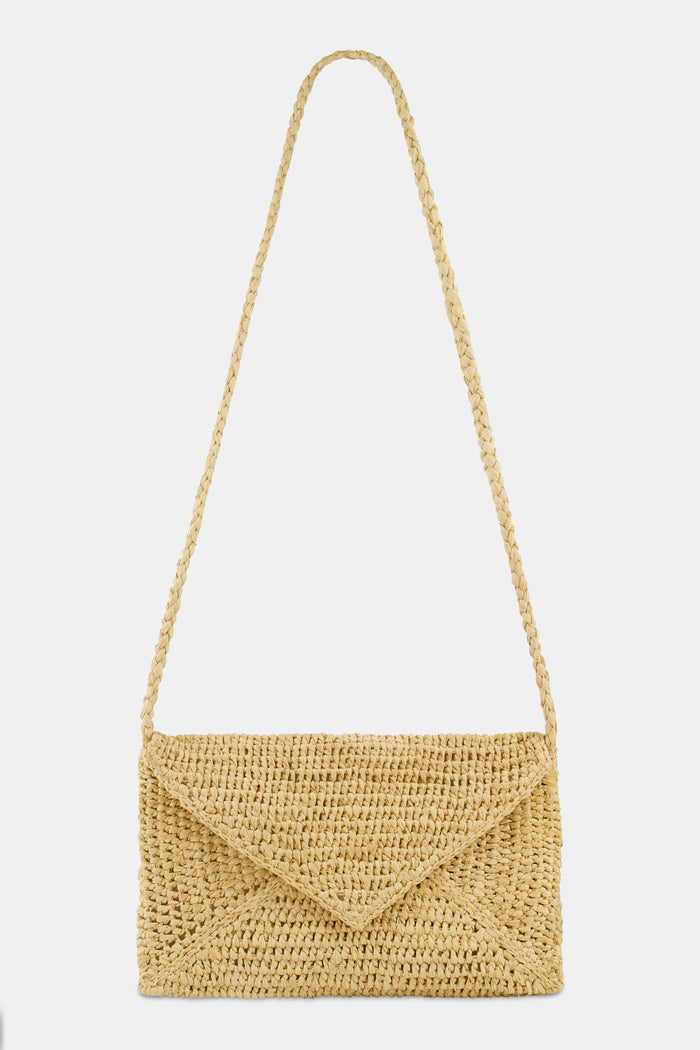 A woman in a light pink, short-sleeve, ruffled dress with a subtle pattern carries the Hat Attack Emmie Envelope Clutch, a woven beige raffia bag with flap closure. The image is cropped below her eyes.