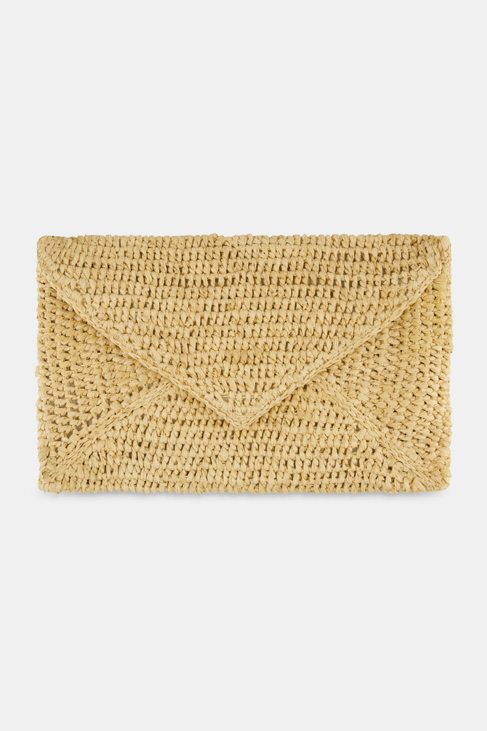 A woman in a light pink, short-sleeve, ruffled dress with a subtle pattern carries the Hat Attack Emmie Envelope Clutch, a woven beige raffia bag with flap closure. The image is cropped below her eyes.