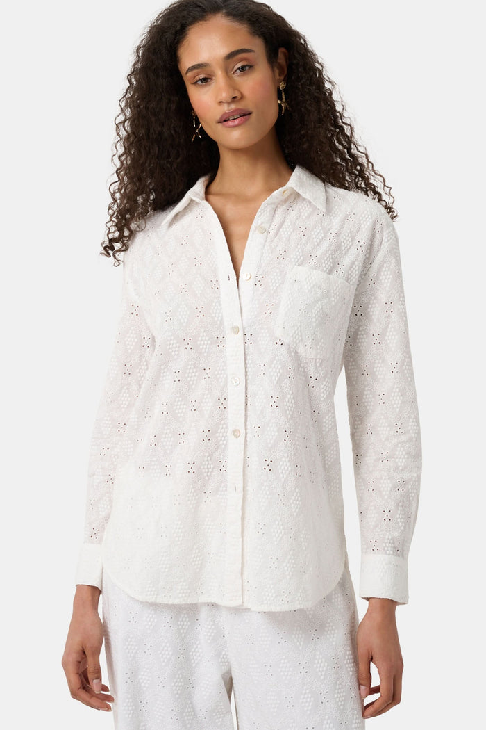 A woman with long curly hair wears the Roller Rabbit Eyelet Lattice Boyfriend Shirt in white, featuring a front pocket, paired with matching white pants against a plain background.