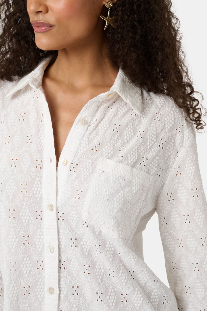 A woman with long curly hair wears the Roller Rabbit Eyelet Lattice Boyfriend Shirt in white, featuring a front pocket, paired with matching white pants against a plain background.
