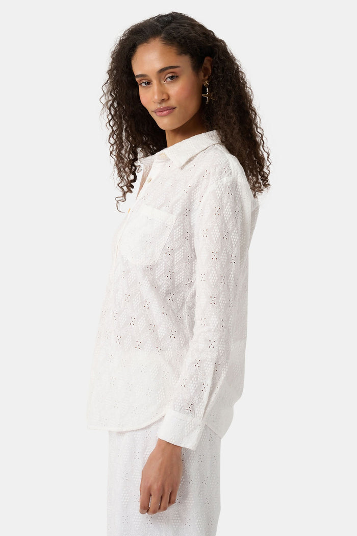 A woman with long curly hair wears the Roller Rabbit Eyelet Lattice Boyfriend Shirt in white, featuring a front pocket, paired with matching white pants against a plain background.
