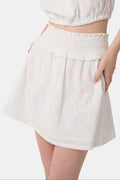 Wearing the Roller Rabbit Eyelet Lattice Erin Skirt with a smocked waist and delicate embroidery, paired with a matching white cropped top, their hand rests on their hip.