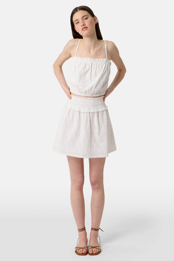 Wearing the Roller Rabbit Eyelet Lattice Erin Skirt with a smocked waist and delicate embroidery, paired with a matching white cropped top, their hand rests on their hip.