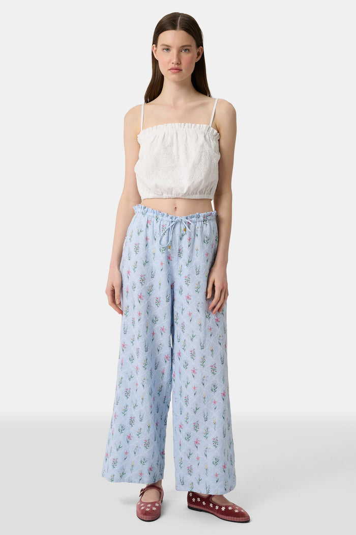 A woman wears the Roller Rabbit Eyelet Lattice Leah Top—white with thin straps and ruffled, elastic detail—paired with a matching high-waisted skirt. This stylish summer look is set against a plain white background.
