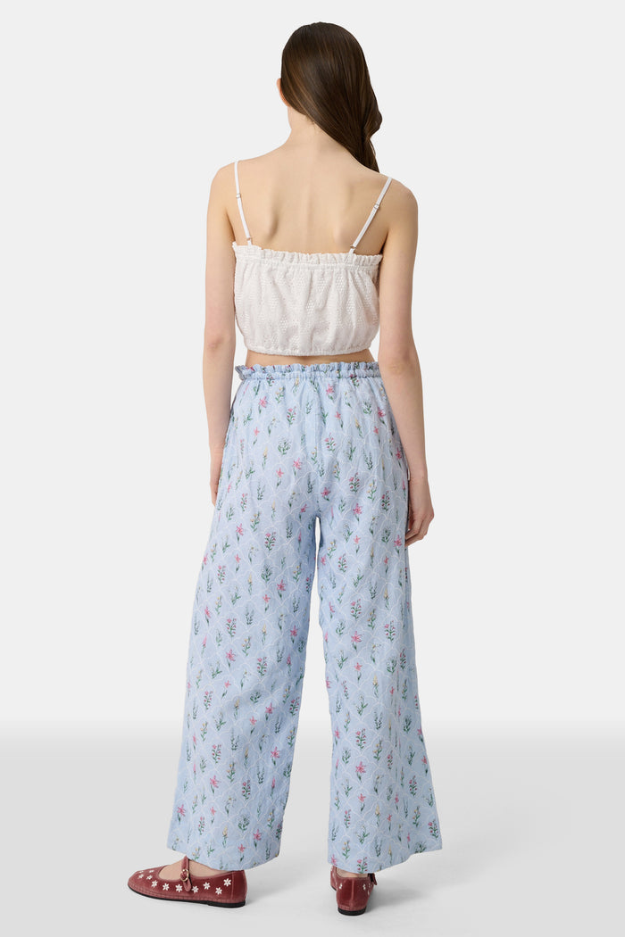 A woman wears the Roller Rabbit Eyelet Lattice Leah Top—white with thin straps and ruffled, elastic detail—paired with a matching high-waisted skirt. This stylish summer look is set against a plain white background.