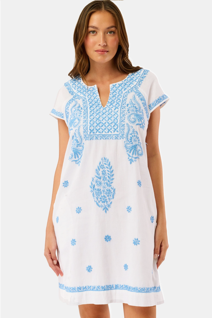 A woman wears the Roller Rabbit Faith Dress, a short-sleeved white cotton midi dress with blue embroidery, standing facing forward with hands by her sides against a plain light background.