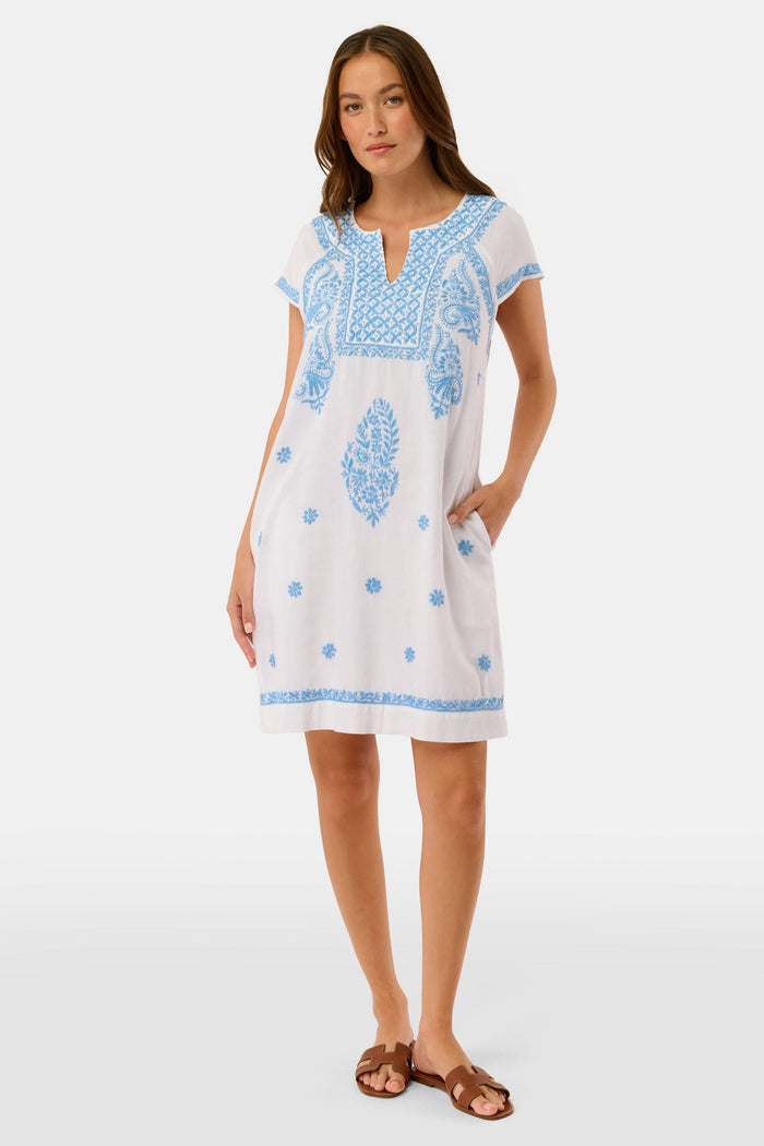 A woman wears the Roller Rabbit Faith Dress, a short-sleeved white cotton midi dress with blue embroidery, standing facing forward with hands by her sides against a plain light background.