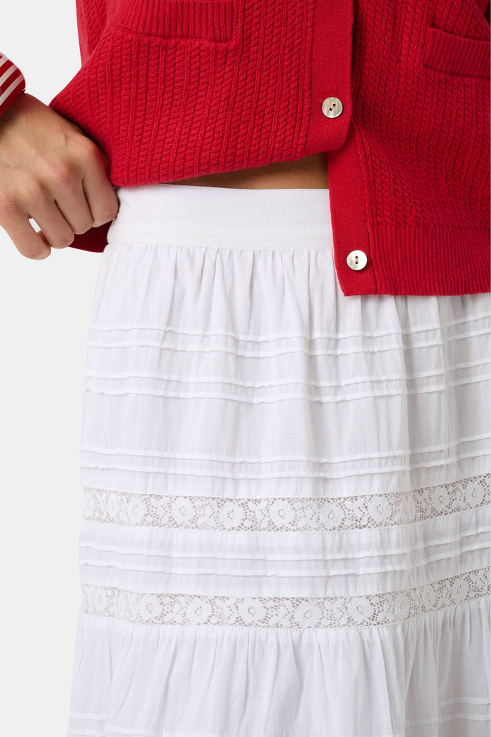 A person wears a red cardigan, the Florence Lace Carlisa Skirt by Roller Rabbit, brown slide sandals, and red, white, and blue bangle bracelets against a plain white background.