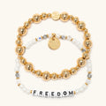 Freedom Bracelet Set from the Project HEAL giveback collection, the gold plated Gold Bubbles bracelet base stacked above the Freedom bracelet in white faux pearl and crystal beads