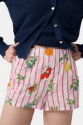 A person stands hands on hips, wearing a navy blue cardigan and Roller Rabbit Fruits D'Ete Sonny Boxer in white cotton voile, featuring pink stripes plus colorful strawberries, oranges, pears, and floral patterns.
