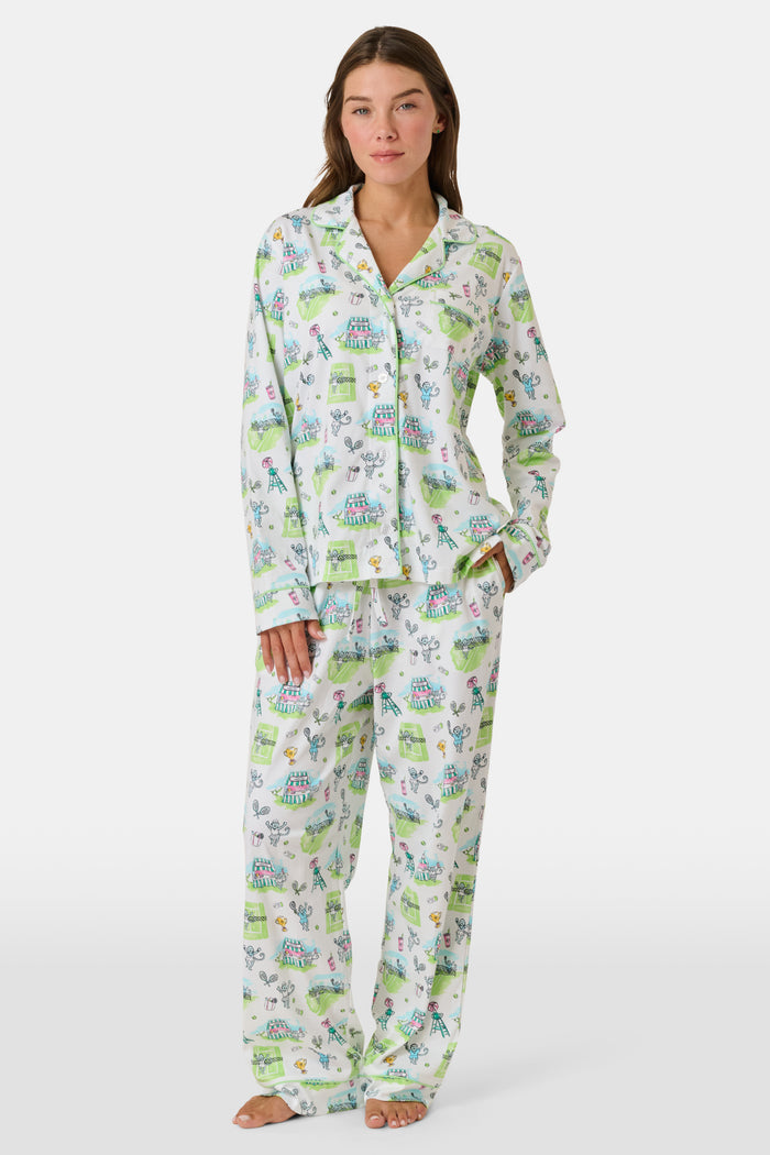 Introducing the Game, Set, Monkey Long Sleeve Polo Pajamas by Roller Rabbit—a cozy white pajama set expertly crafted from soft Pima Cotton. The set features a playful Game Set Monkey print with vibrant green, blue, and yellow animal and nature illustrations. Designed with long sleeves, a button-up polo top, and comfortable drawstring waist pants, this delightful set is showcased against a plain light background.