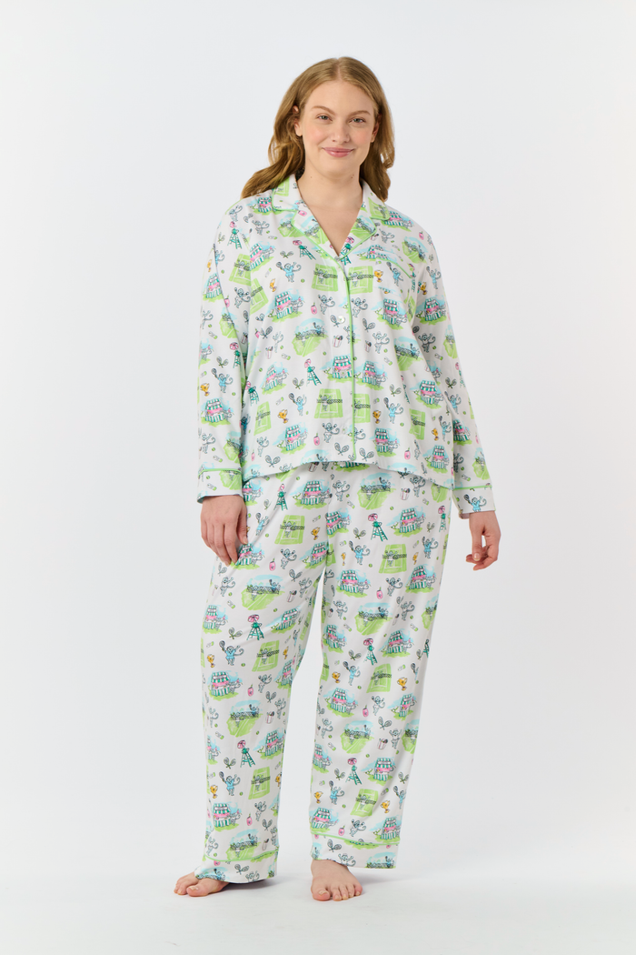Introducing the Game, Set, Monkey Long Sleeve Polo Pajamas by Roller Rabbit—a cozy white pajama set expertly crafted from soft Pima Cotton. The set features a playful Game Set Monkey print with vibrant green, blue, and yellow animal and nature illustrations. Designed with long sleeves, a button-up polo top, and comfortable drawstring waist pants, this delightful set is showcased against a plain light background.