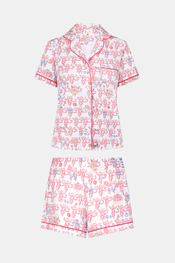 Introducing the Roller Rabbit Gamma Phi Beta Monkey Polo Pajamas: a short-sleeve Pima cotton set featuring a button-up top and matching shorts, adorned with a whimsical pink and blue monkey pattern and red trim on a crisp white background.