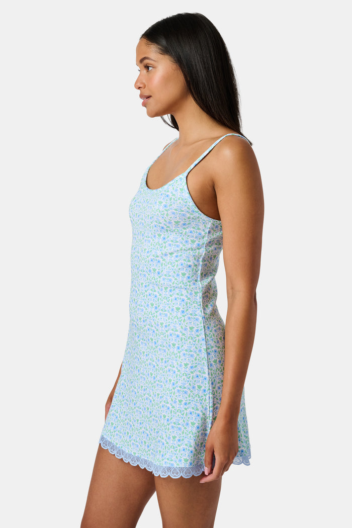 The Roller Rabbit Garden Gate Floral Daniela Slip Dress features a sleeveless, knee-length silhouette with thin straps, a blue and green floral Garden Gate print, and blue lace trim at the hem, shown against a plain white background.