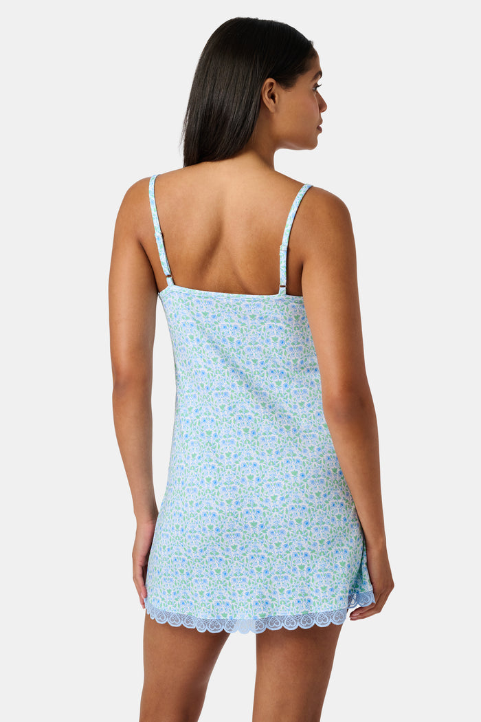 The Roller Rabbit Garden Gate Floral Daniela Slip Dress features a sleeveless, knee-length silhouette with thin straps, a blue and green floral Garden Gate print, and blue lace trim at the hem, shown against a plain white background.