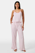 The Garden Gate Floral Lily Set by Roller Rabbit features a pink and white women's loungewear set with a sleeveless, V-neck camisole and loose pants. Made from soft Pima cotton, both pieces showcase a delicate floral pattern and light pink trim. The comfy tank and pants include a drawstring waist and ruffled hems for added comfort and style.