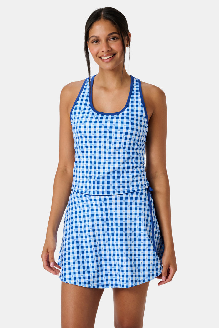 A person wears the Roller Rabbit Gingham Hearts Bella Tank, a blue-and-white checkered racerback style with small heart details. The image is cropped at the shoulders and midsection, showing part of the matching skirt and the person’s head.