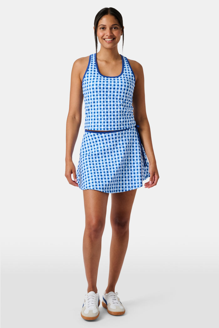 A person wears the Roller Rabbit Gingham Hearts Bella Tank, a blue-and-white checkered racerback style with small heart details. The image is cropped at the shoulders and midsection, showing part of the matching skirt and the person’s head.