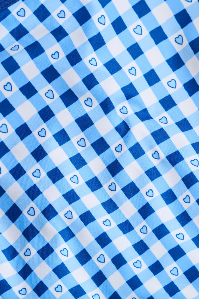 A person wears the Roller Rabbit Gingham Hearts Bella Tank, a blue-and-white checkered racerback style with small heart details. The image is cropped at the shoulders and midsection, showing part of the matching skirt and the person’s head.