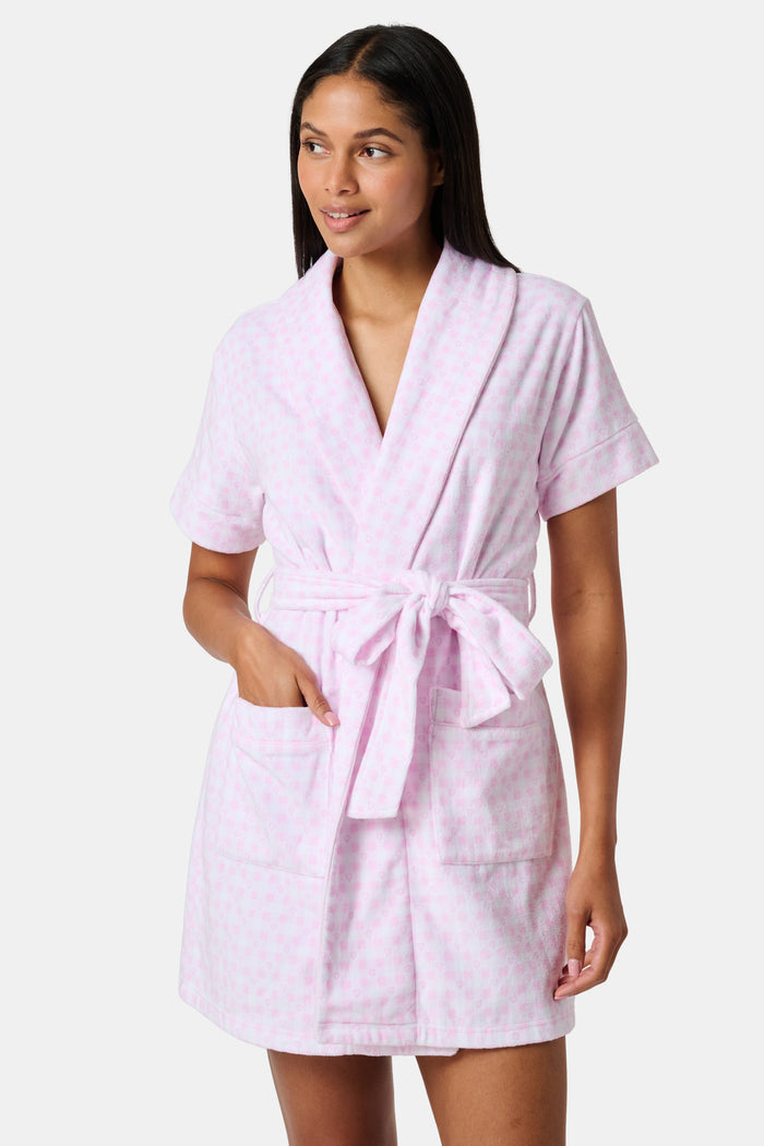 The Roller Rabbit Gingham Hearts Brooks Robe features a light pink gingham pattern with subtle hearts, crafted from soft cotton. This short-sleeve robe includes front pockets and a matching waist tie, and is displayed against a plain white background.